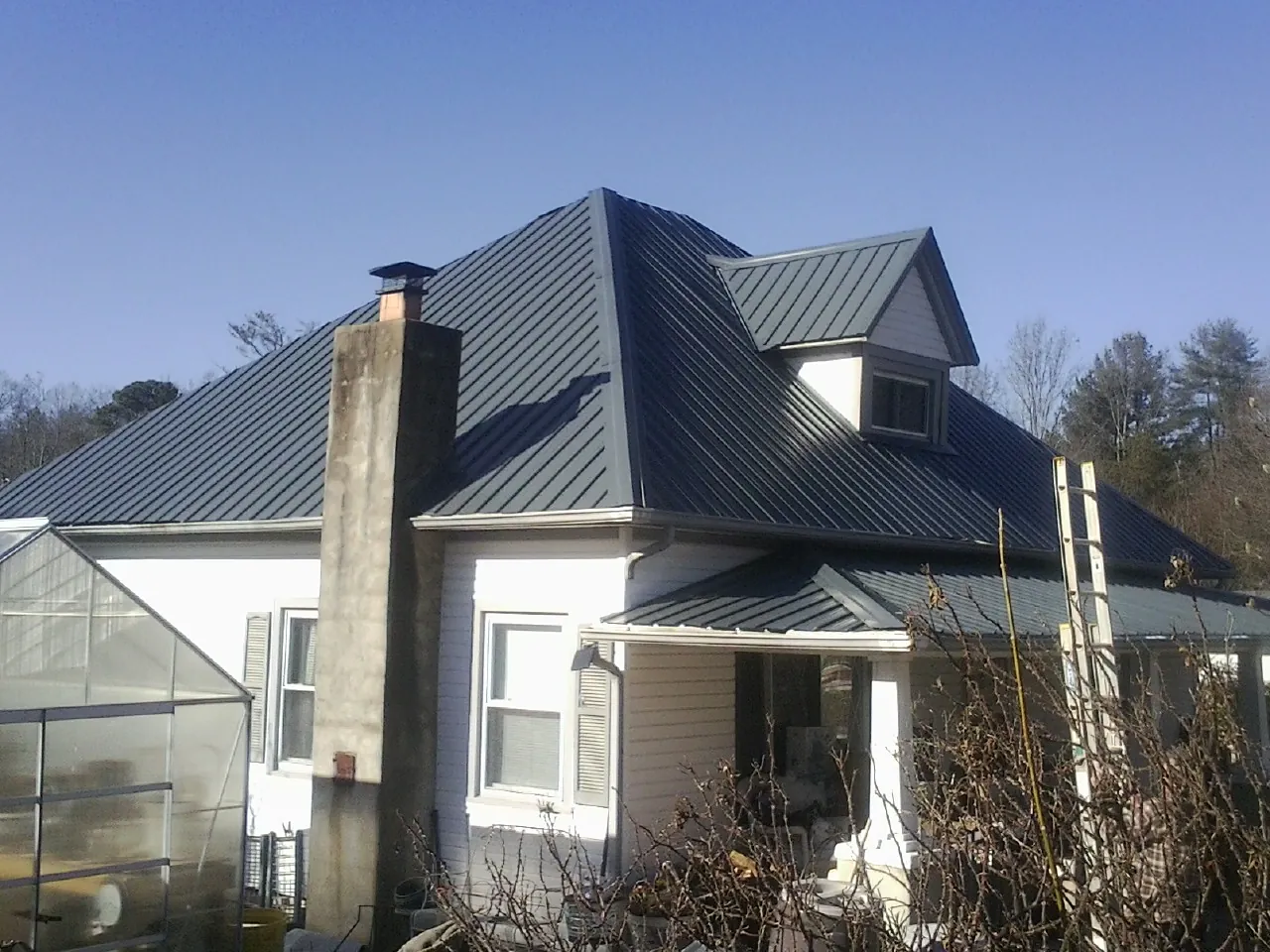Dark blue standing seam metal roof on a white farmhouse with dormer — Slate & Tile Roof Repair by Roofing Brothers in Avenel