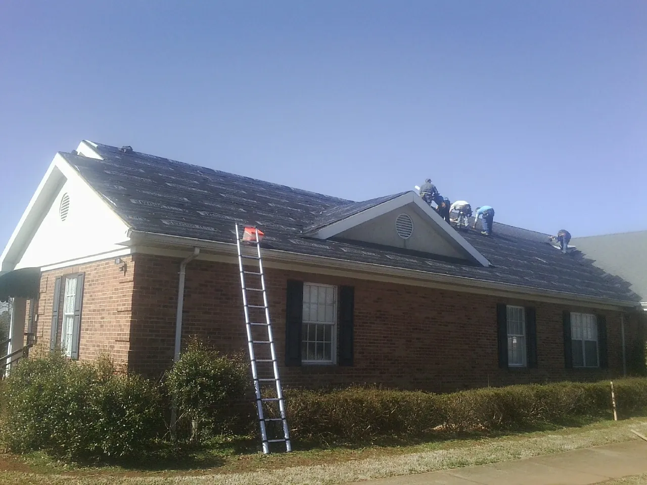 Crew tearing shingles off a brick ranch roof with a ladder set — Emergency Roof Repair work by our crew in Avenel