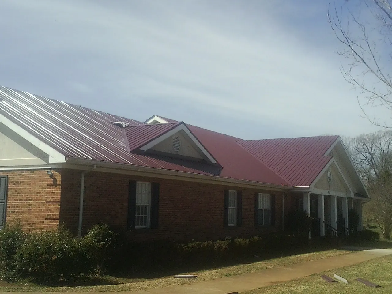 Red metal roof with gabled entries on a long brick building, from a Hail Damage Roof Repair job in Avenel