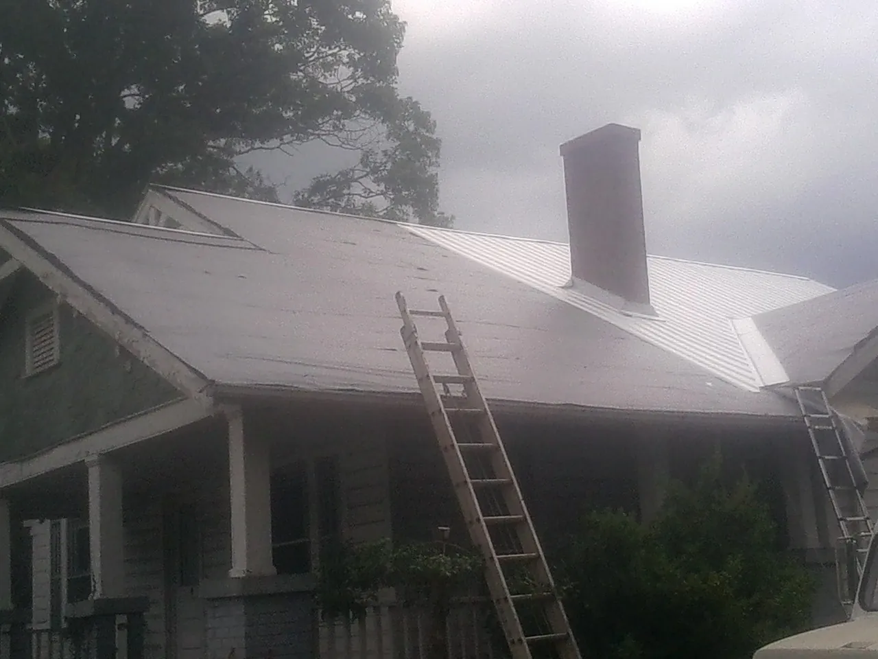 Ladders against a metal roof on an older home with a brick chimney in Avenel