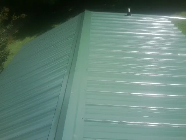New green metal panels meeting at the ridge of a roof — Flat Roof Repair work by our crew in Avenel