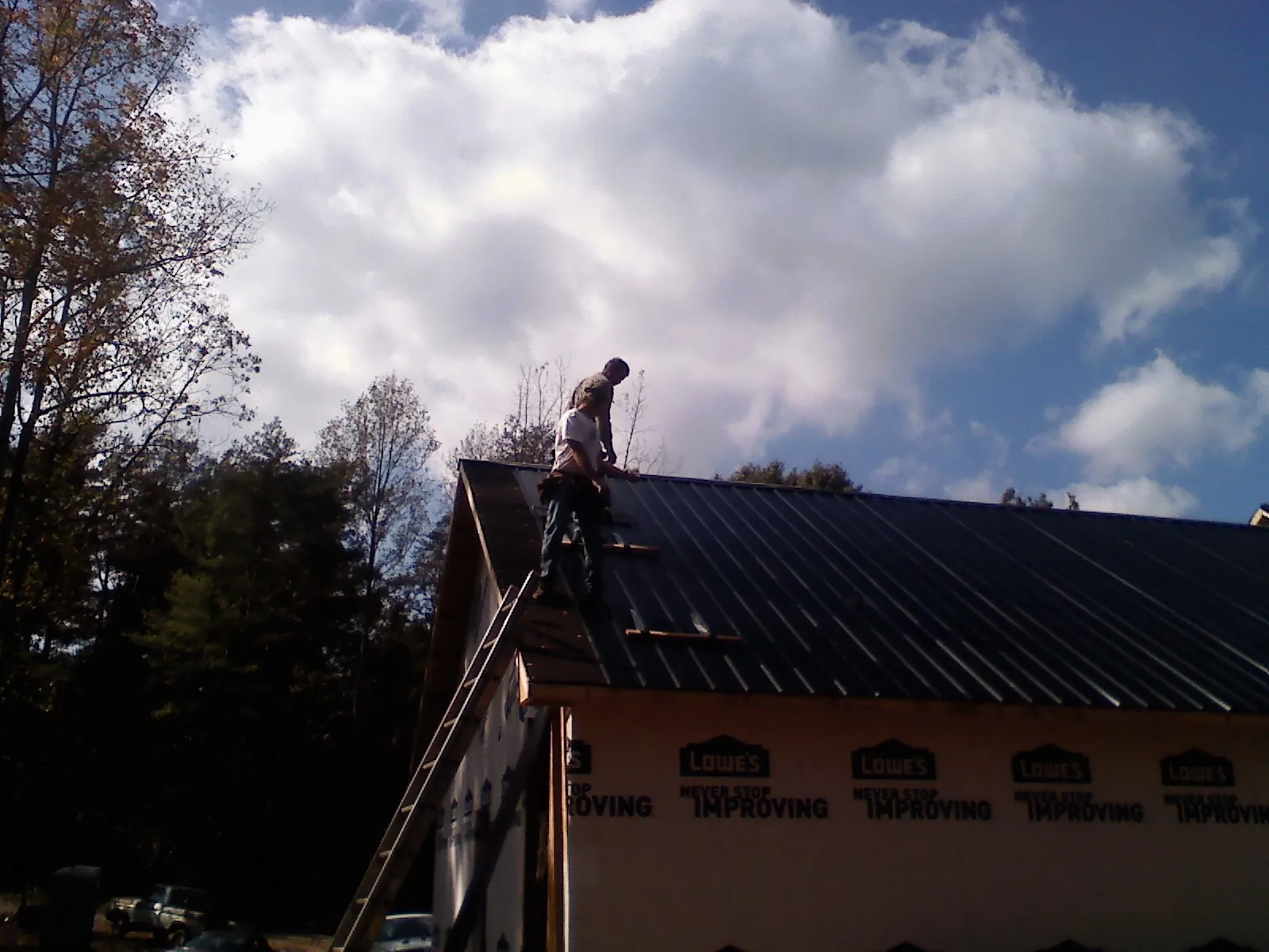 Roofer fastening dark metal panels high against a cloudy sky, from a Roof Inspection job in Avenel