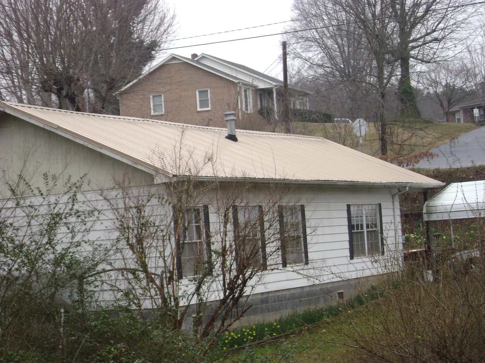 Tan metal roof on a white sided house set into a hillside — Commercial Roofing by Roofing Brothers in Avenel
