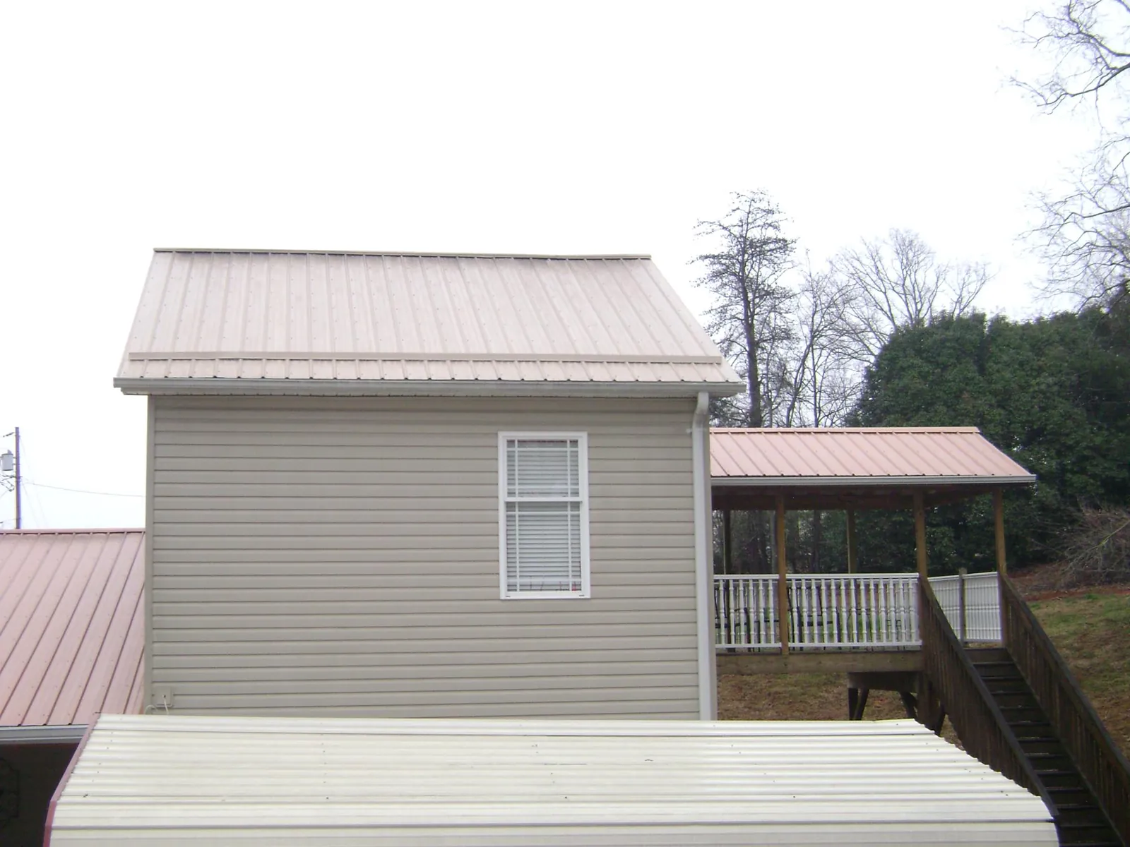 Tan metal roofs on a two story addition and attached porch, from a Roof Replacement job in Avenel